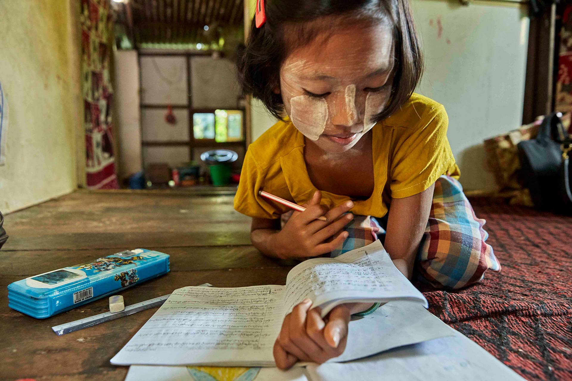 Hnin is from Myanmar and is living with type 1 diabetes. She is doing homework on the floor in her house. 
