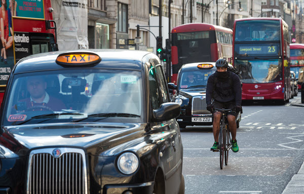 London street view of biker covering his face, surrounded by iconic London taxis and Red Double Decker Buses
