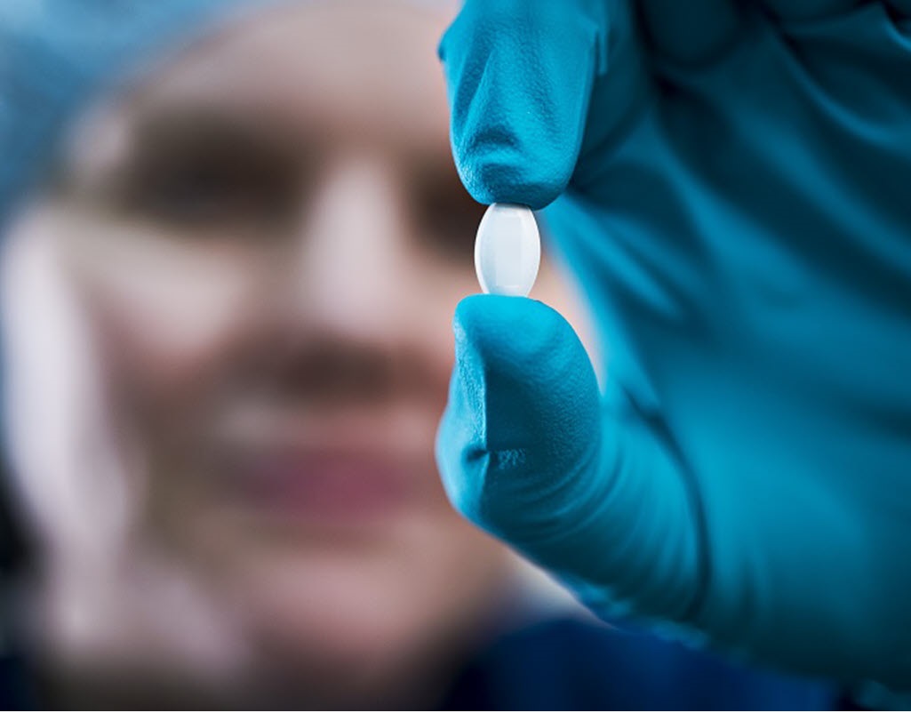 A woman holding up a small pill